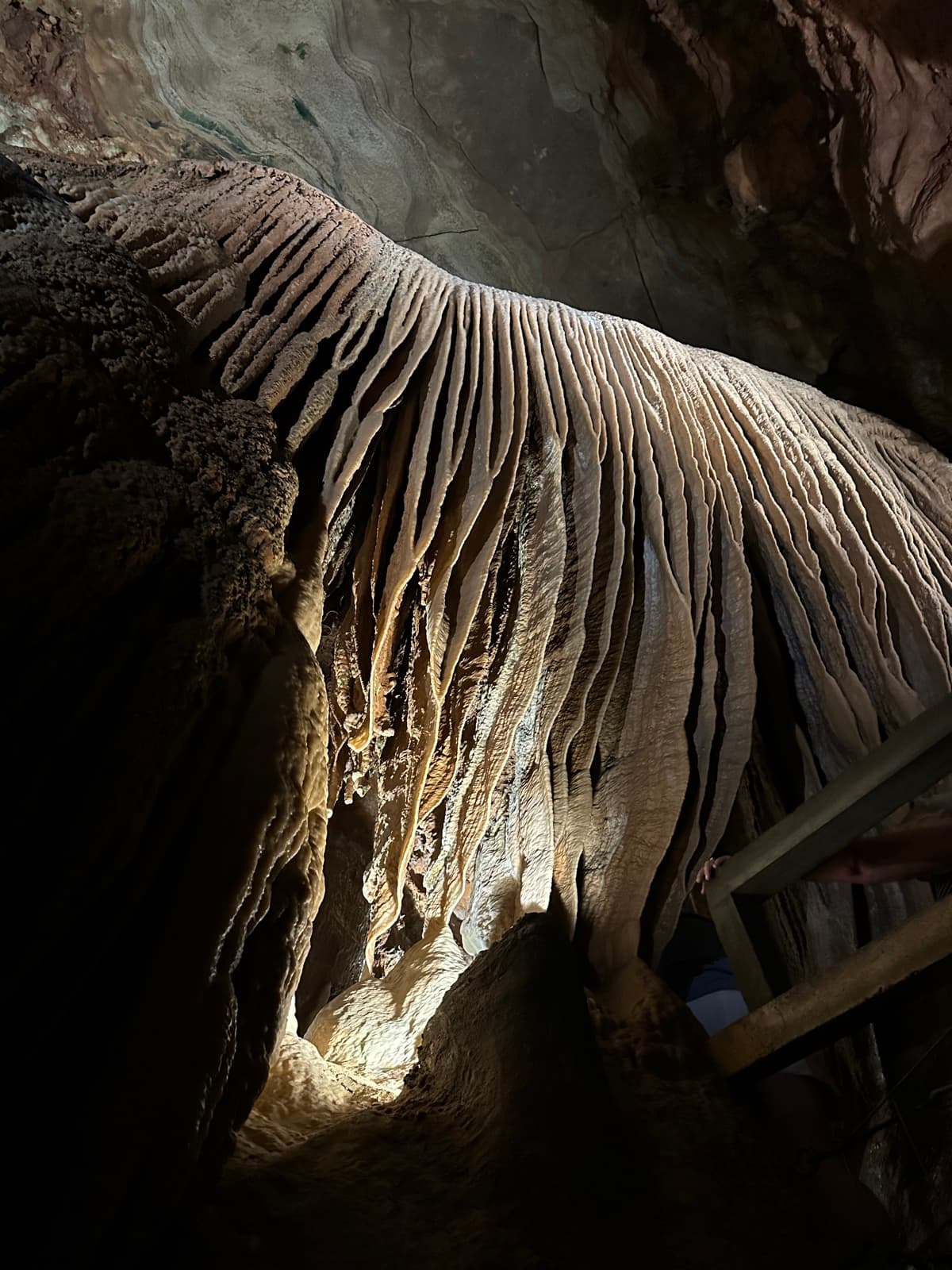 Curtained flowstone formations inside a cave, lit warm from below.