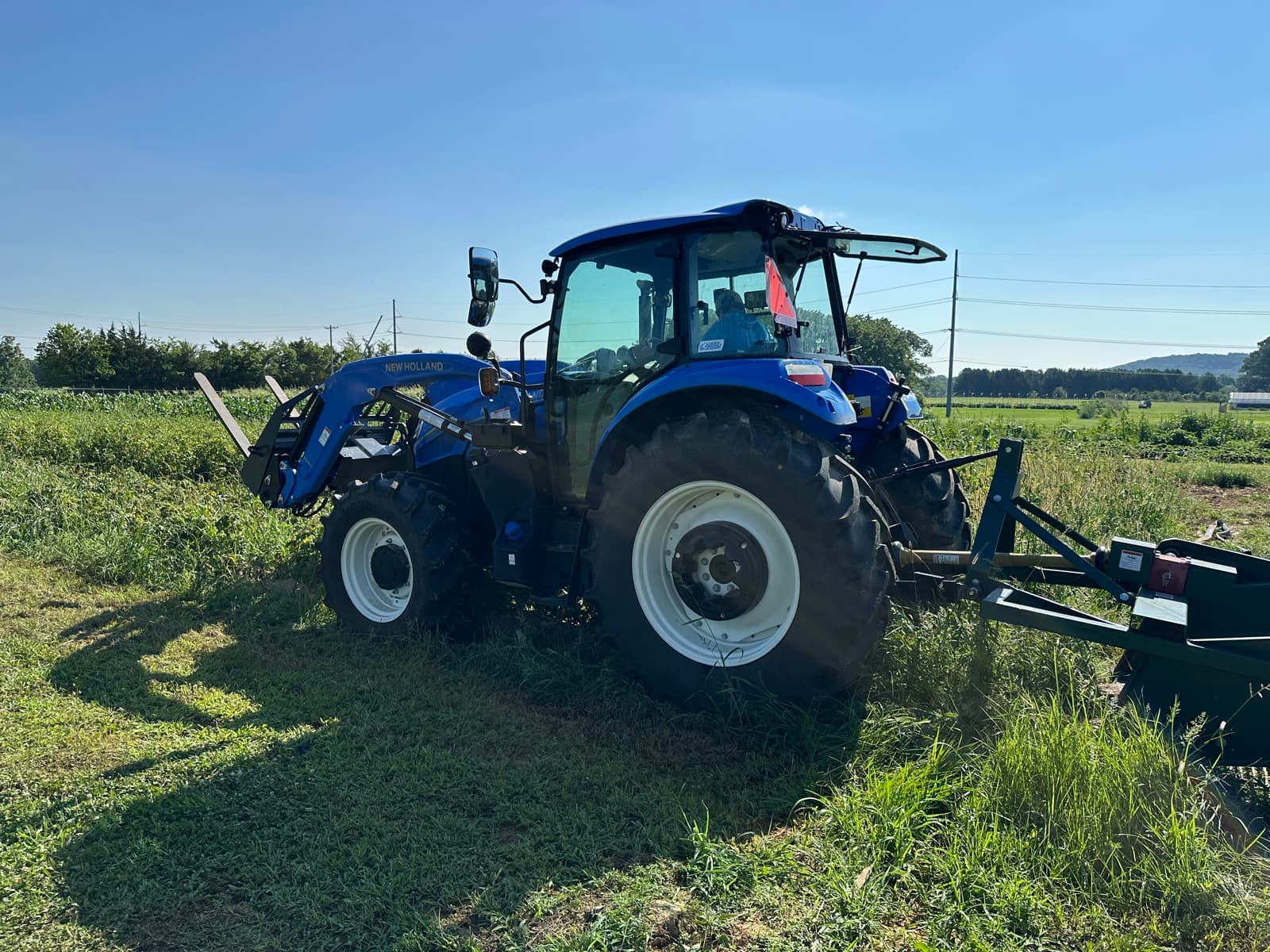 A blue New Holland tractor parked in tall grass at the farm.
