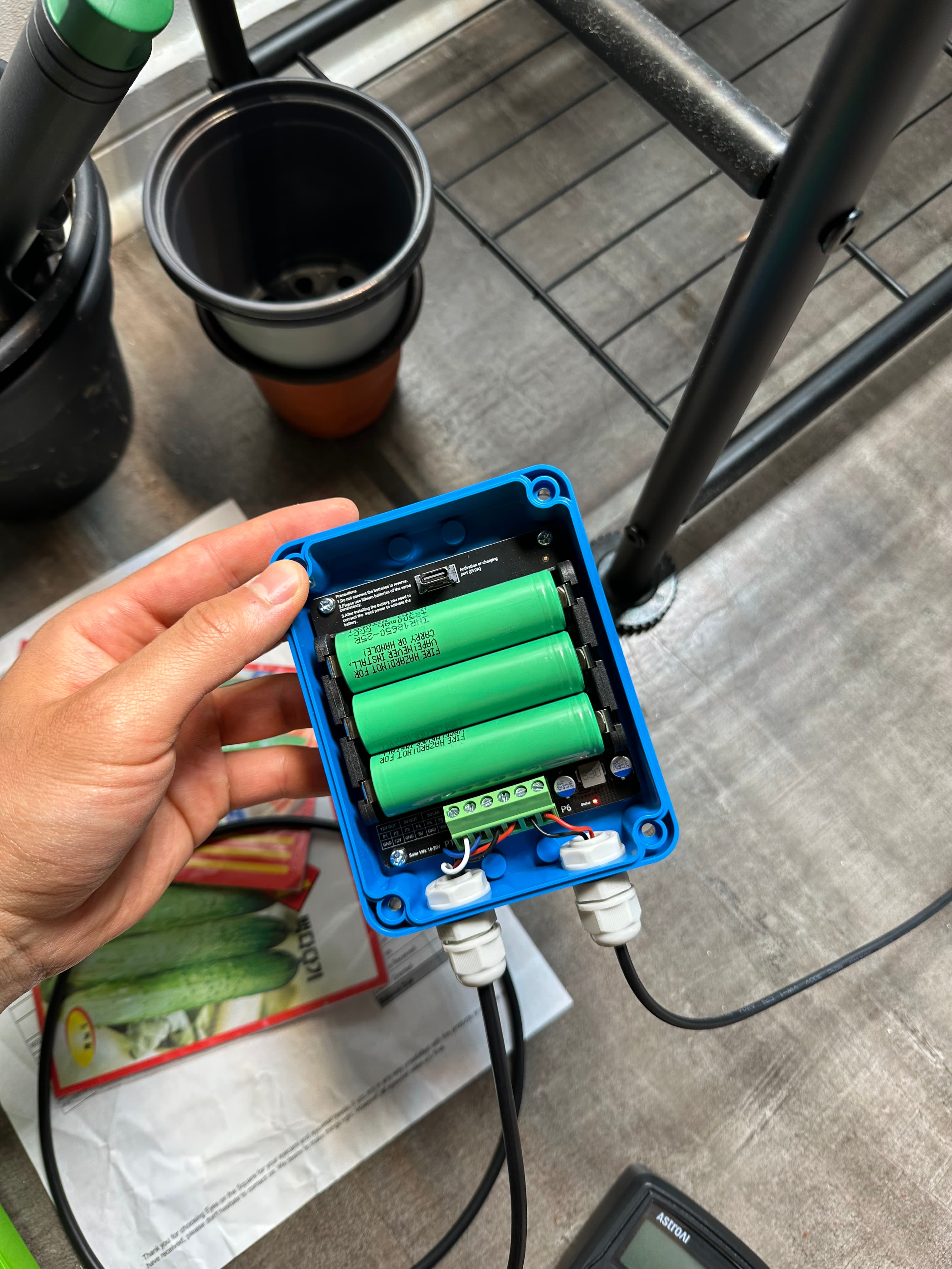 The sealed node in hand — three 18650s, terminal block — beside a seed packet.